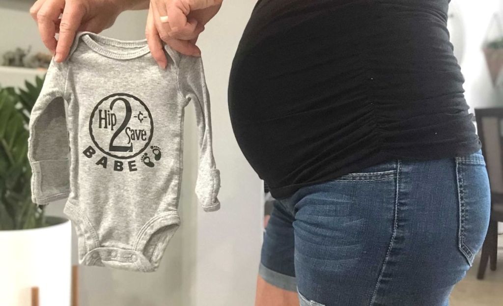 A pregnant woman holding up a personalized onesie