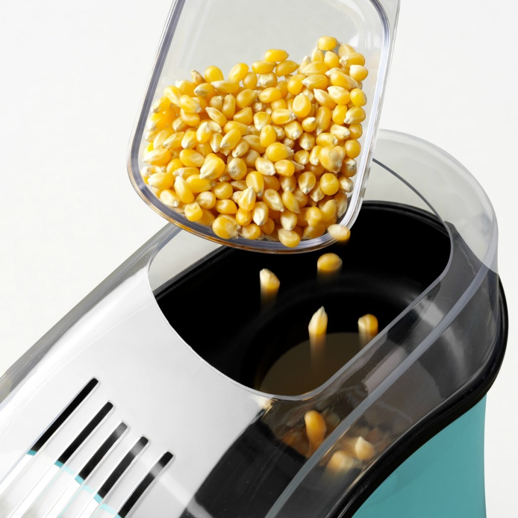 Scoop of popcorn kernels being poured into Nostalgia popcorn maker top