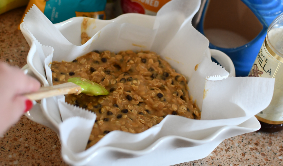 Preparing a pan of peanut butter oatmeal bars made with banana, chocolate chips, and nut or seed butter