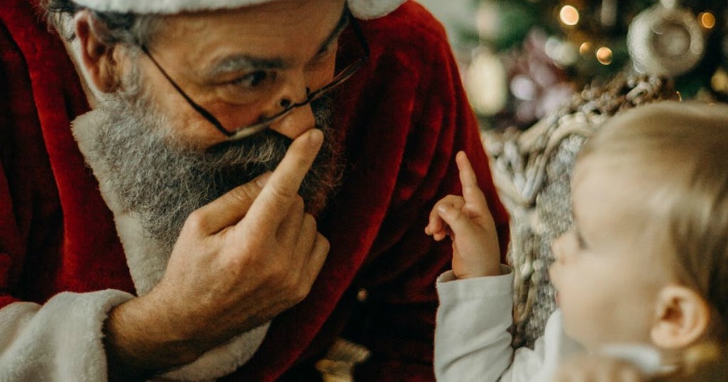Santa Claus pointing to his nose while a baby watches