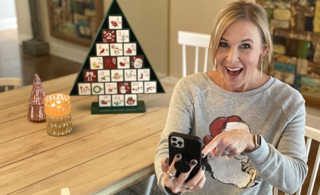 A woman sitting a table holding a phone with cyber monday deals