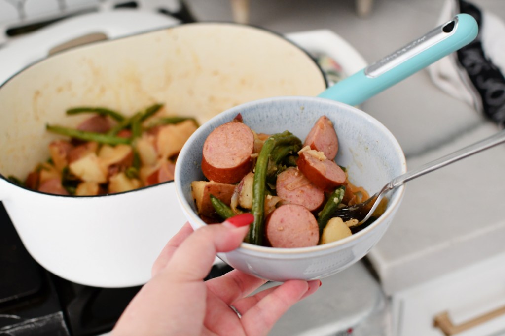 holding a bowl of sausage green beans and potatoes