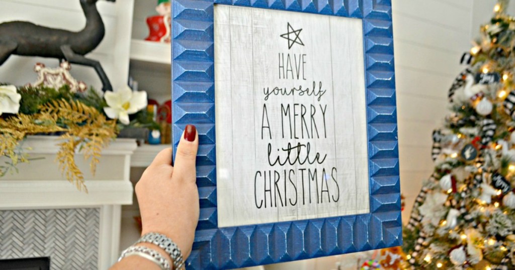 holding Have Yourself a Merry Little Christmas blue frame with Christmas tree in background