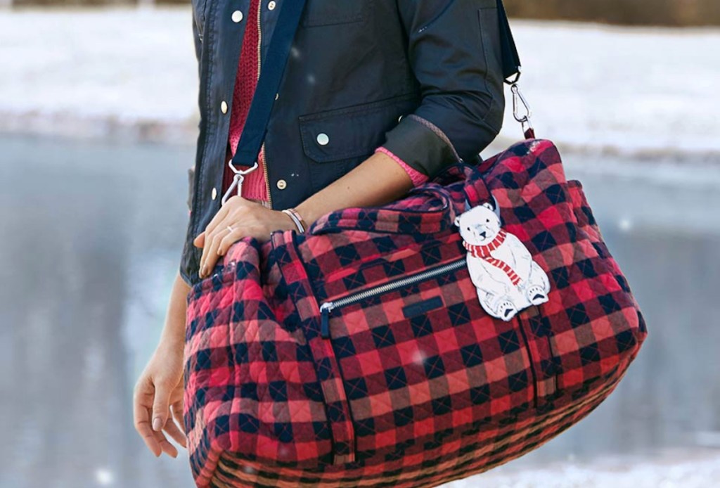 person holding black and red check weekender bag
