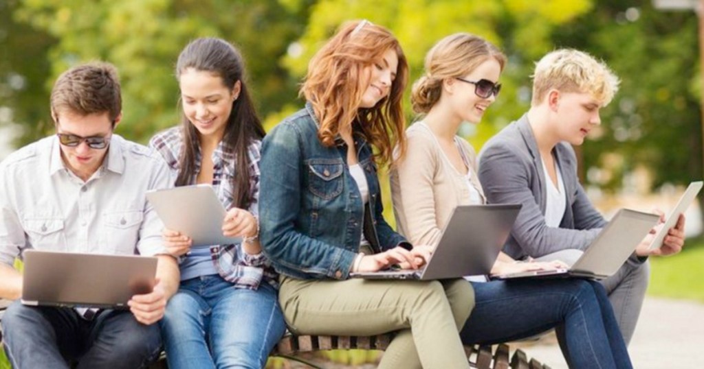 Five college students sitting out side while on their devices
