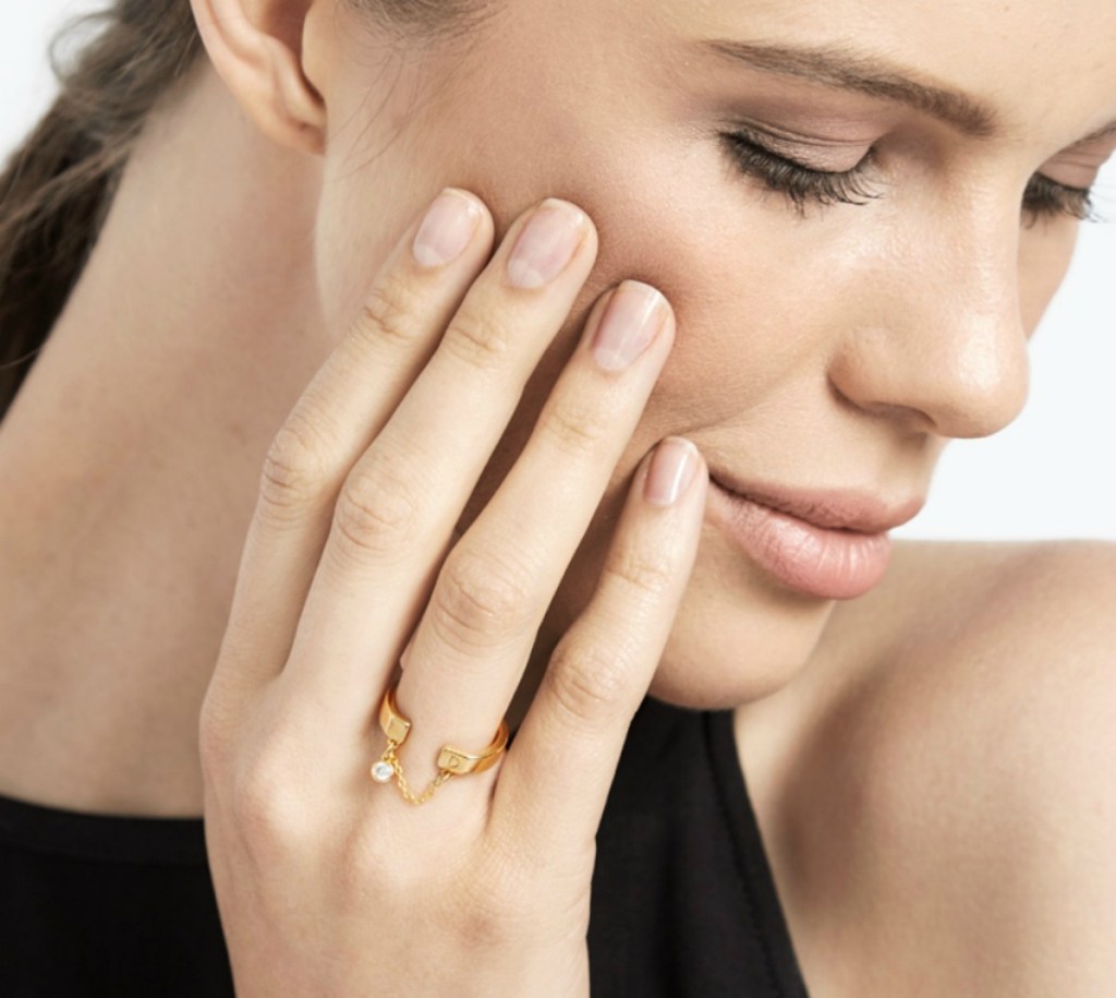 woman wearing a gold initial ring and holding her hand up to her face