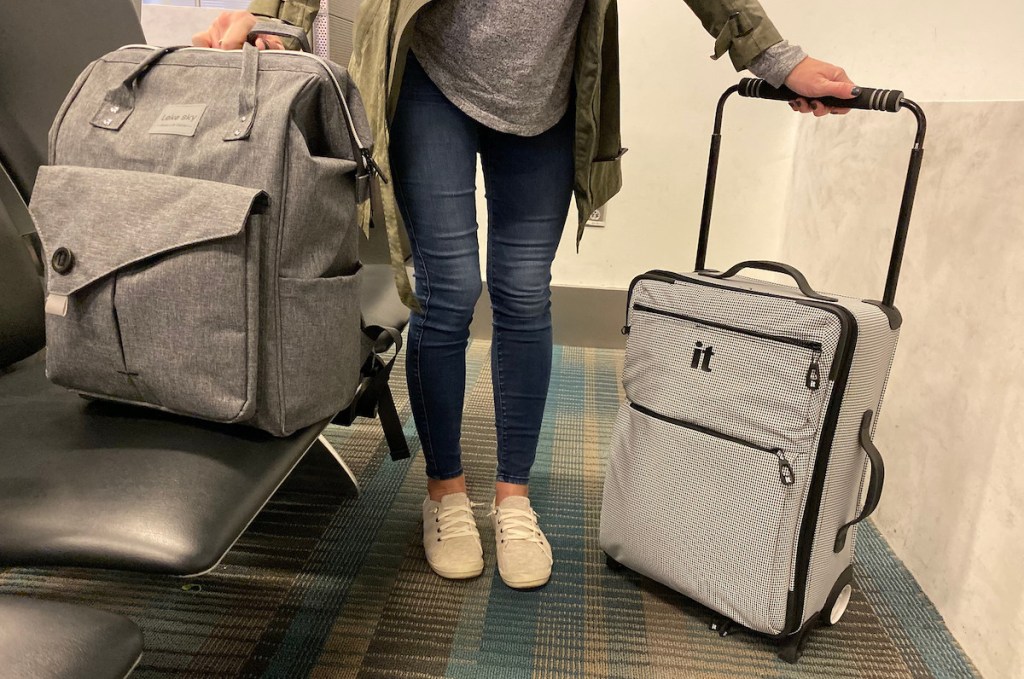 person in airport holding gray bookbag and carry on sized luggage