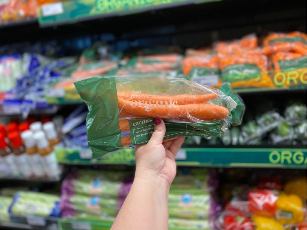 hand holding organic carrots in store with vegetables in background