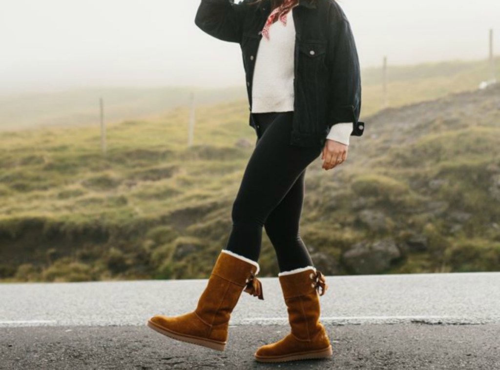 woman walking down a road wearing brown suede boots with bows in the back