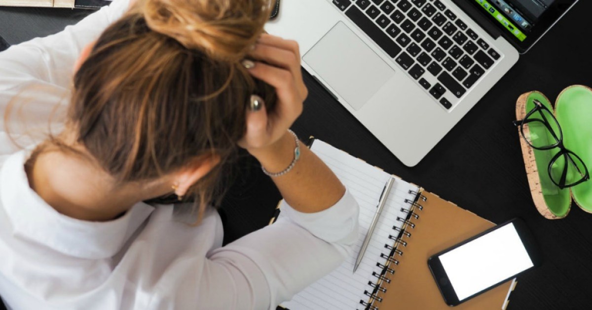 woman holding head in front of Macbook