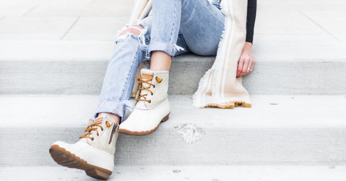 the legs of a lady sitting on cement steps, wearing ripped jeans and White Sperry boots