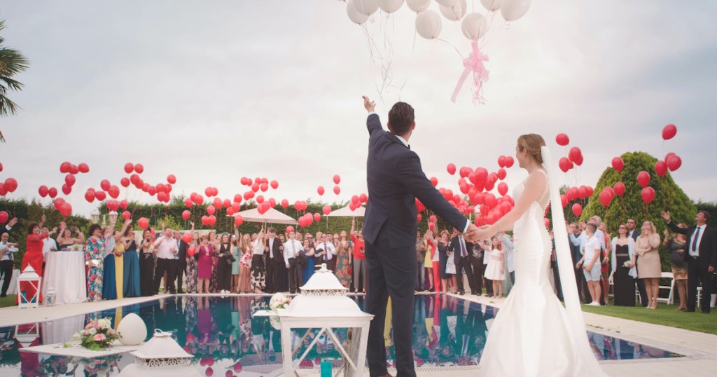 bride and groom standing around pool with their wedding party and tons of balloons
