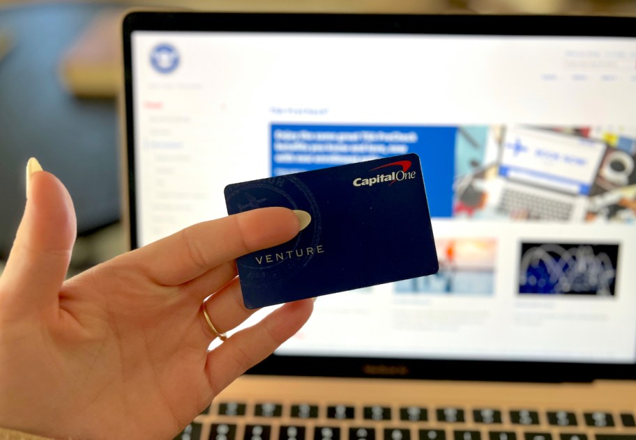 hand holding a capital one venture card in front of laptop