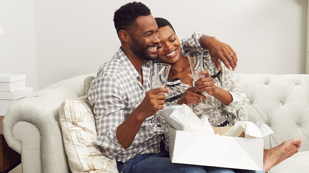 man and woman happy and smiling sitting on couch with champagne glasses