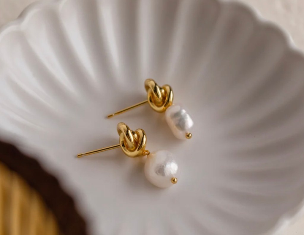 close up of pearl gold knot earrings on scalloped dish
