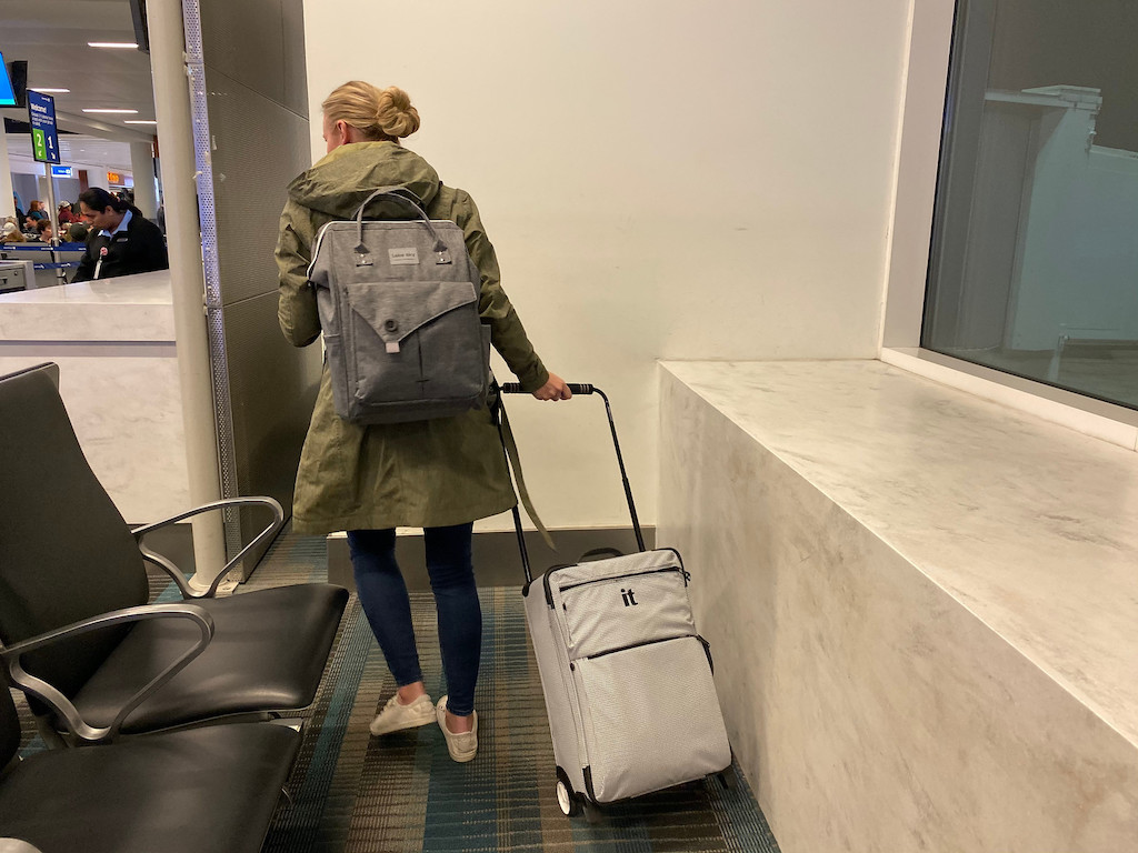 woman with bun and backpack pulling wheeled luggage in airport