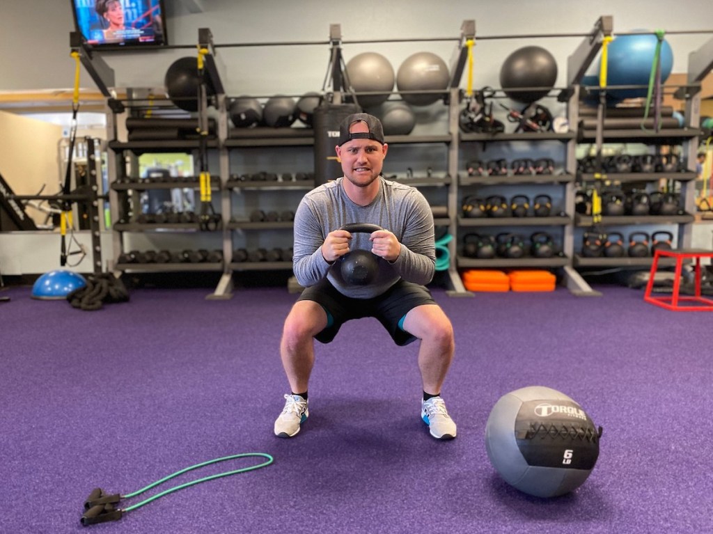 man doing a squat with kettlebell in purple gym
