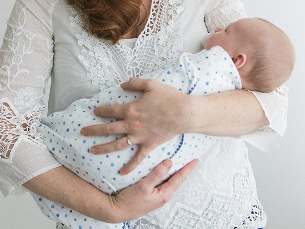 Woman holding a newborn baby wrapped in a cozy blanket with blue polka dots