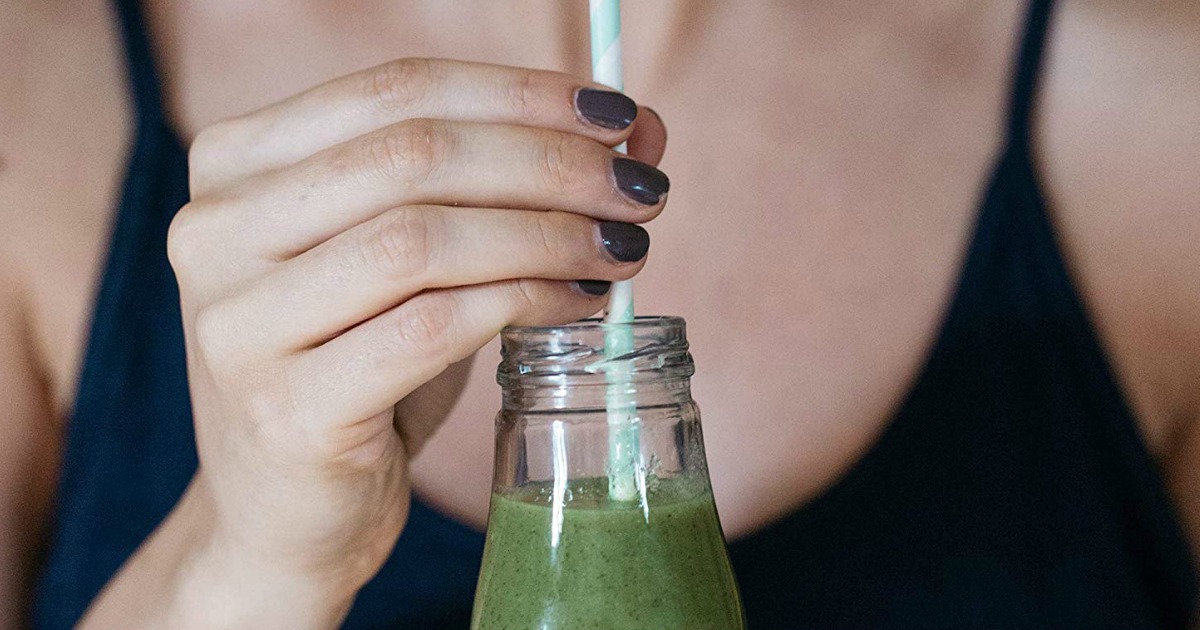 woman sipping green drink from a glass bottle 