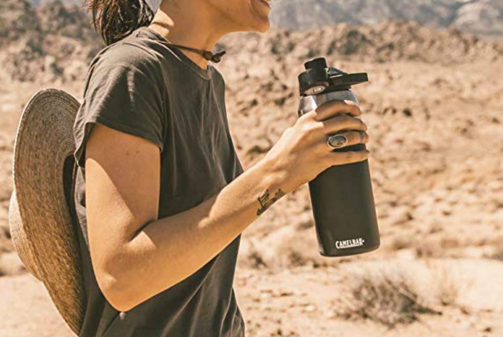 Woman in a dry, dessert area holding a large olive green colored water bottle