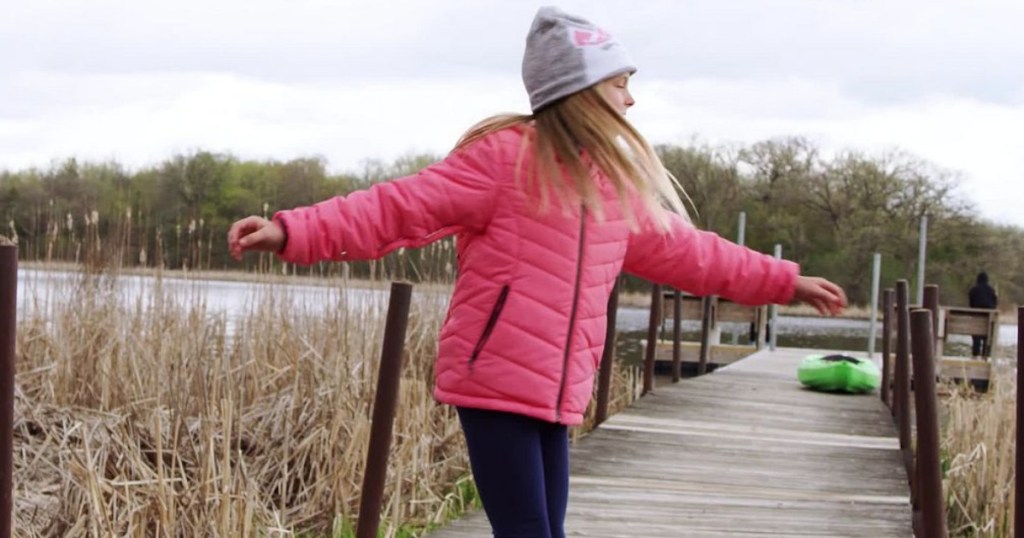 girl spinning on a dock wearing a pink jacket