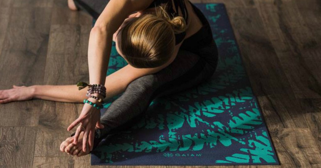 Woman in yoga post on navy blue and green yoga mat on hardwood flooring