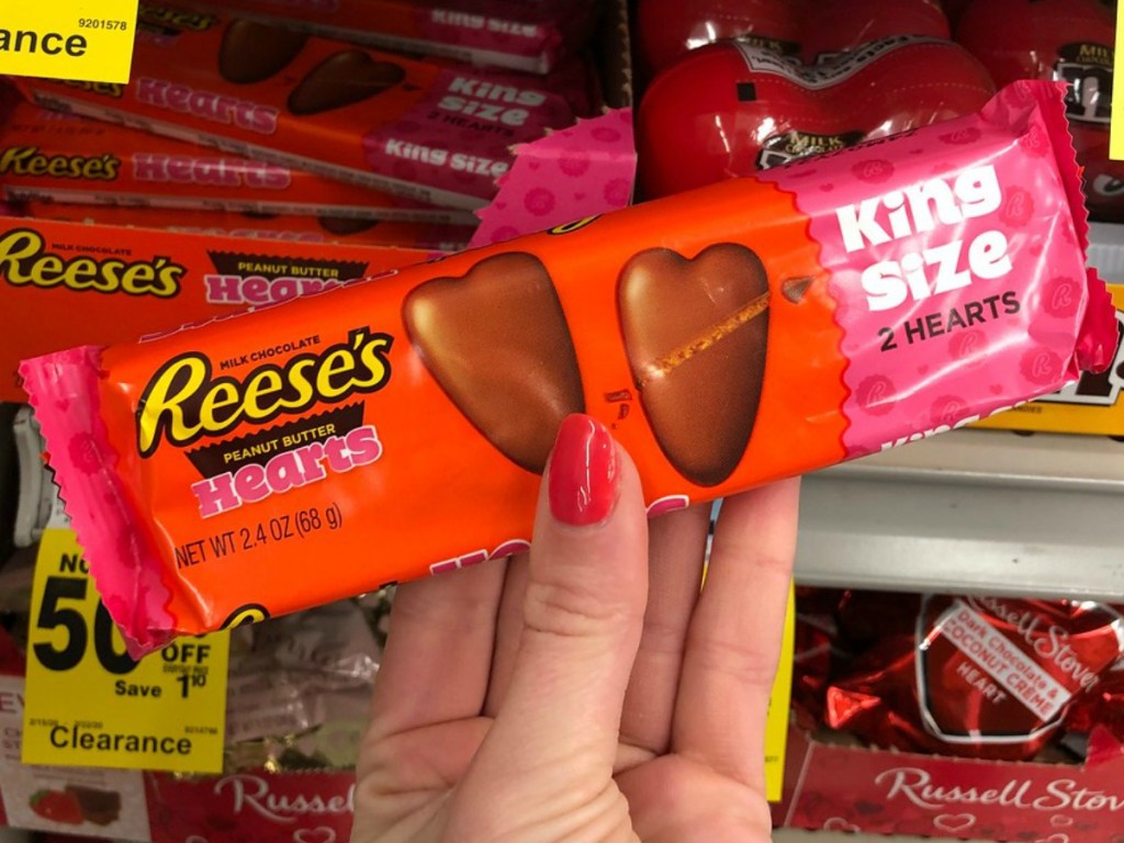 Hand holding king size chocolate covered peanut butter hearts in package near in-store display
