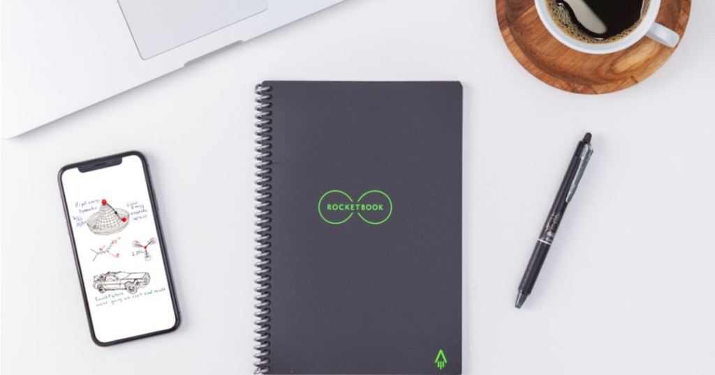 Smart, reusable notebook, smart pen, phone, cup of coffee, and edge of laptop on table.