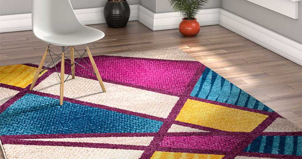 White, Pink, Purple, Blue, and Yellow geo area rug in house with white chair and plant