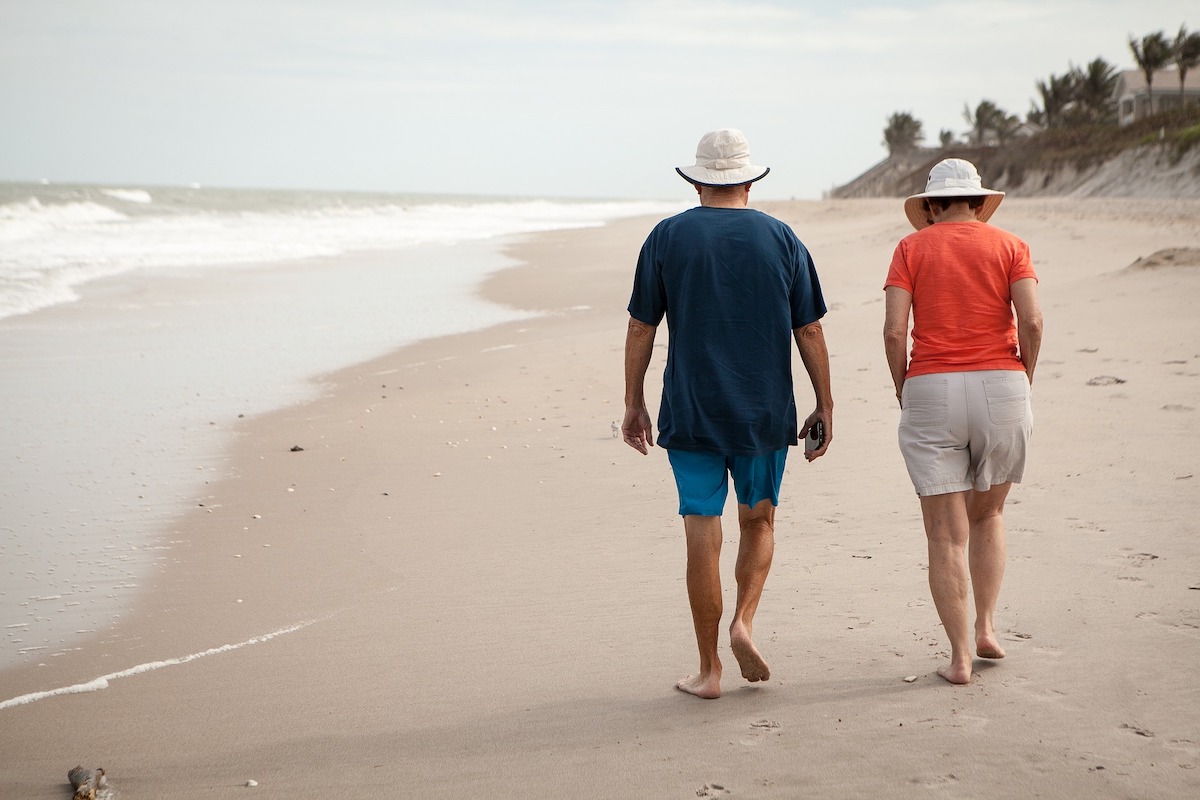 man and woman walking on sandy beach along shoreline