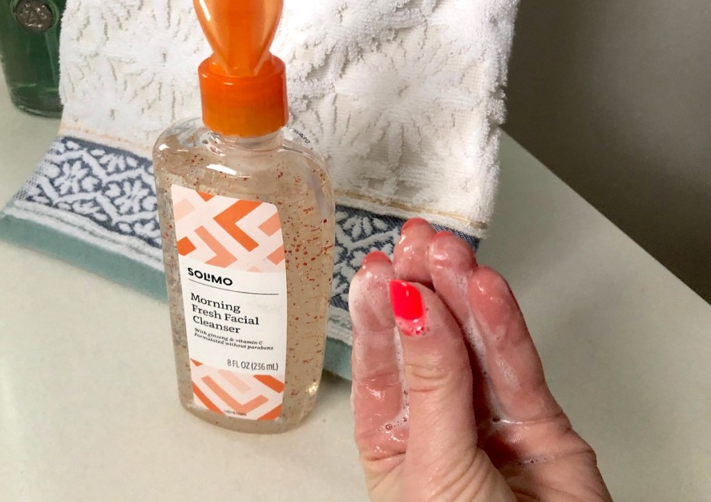 hand rubbing fingers together with soap suds next to bottle of Solimo facial cleanser