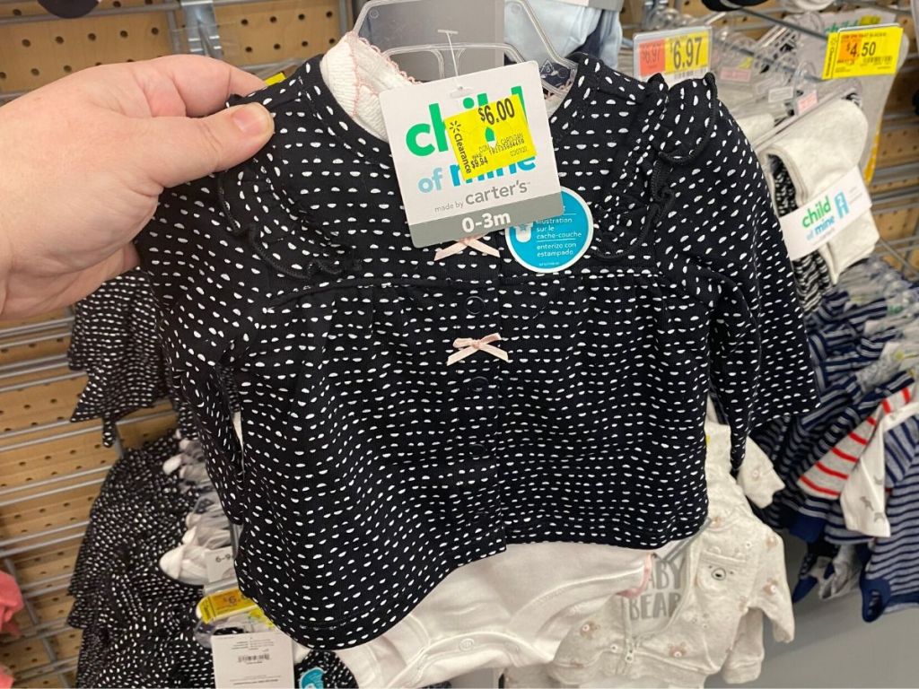 woman's hand holding 3 piece baby girl outfit in store