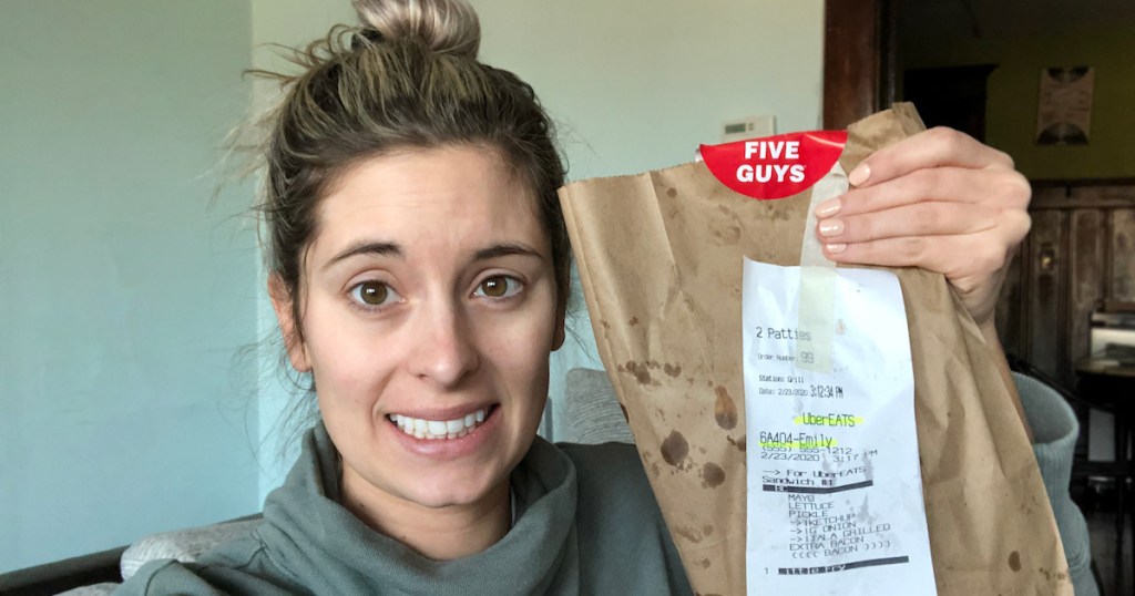 woman holding brown kraft bag of five guys food