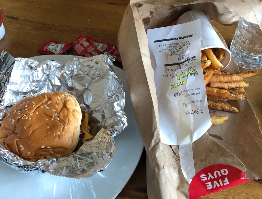burger and fries sitting in foil and brown bag on table
