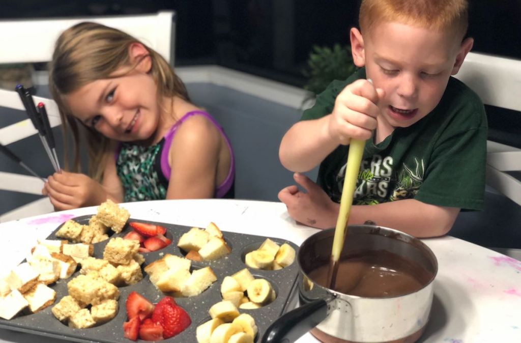 girl and boy sitting with fruit and melted bowl of chocolate fondue