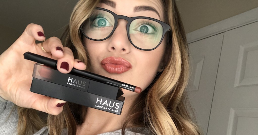 woman holding black haus laboratories makeup wearing glasses
