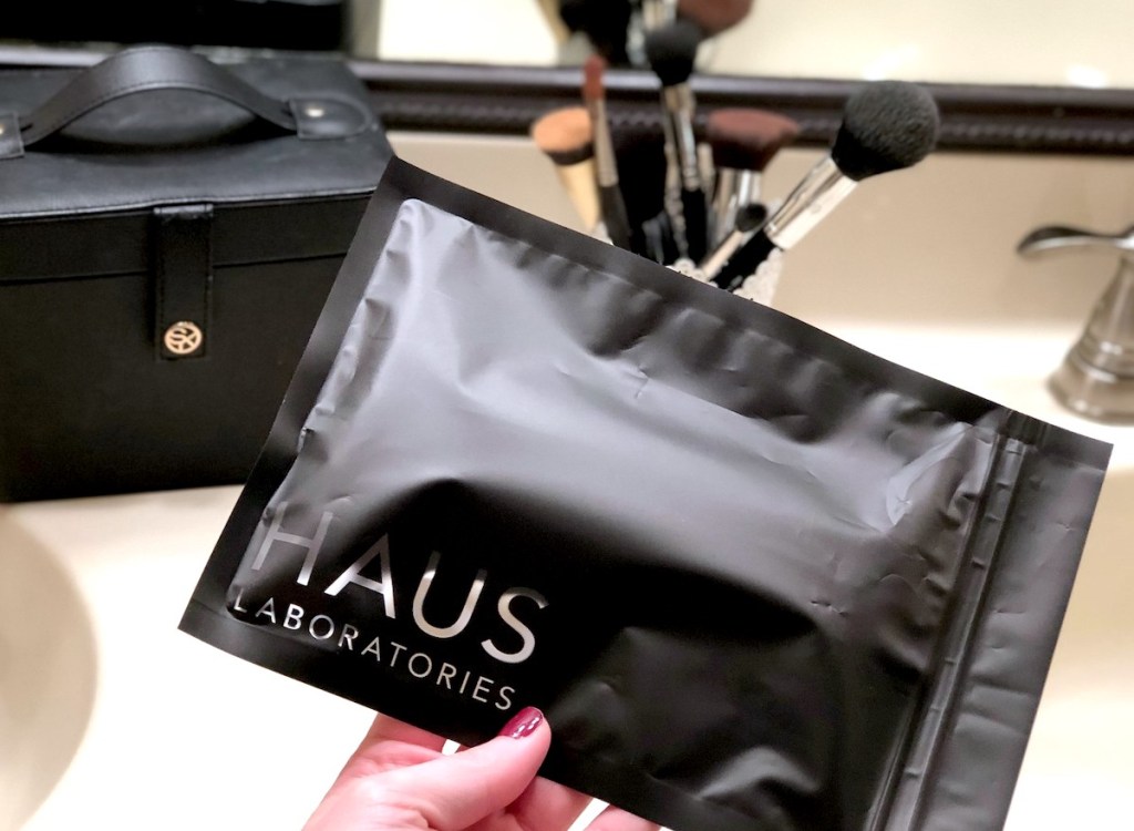 hand holding black haus laboratories bag with makeup brushes in background