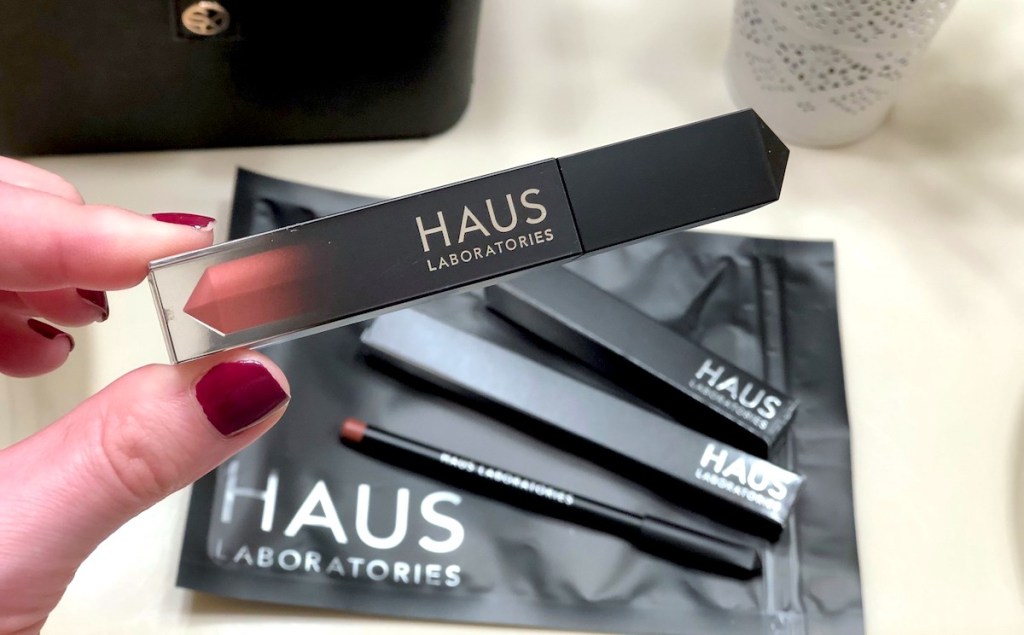 hand holding a haus laboratories lip gloss with makeup in background