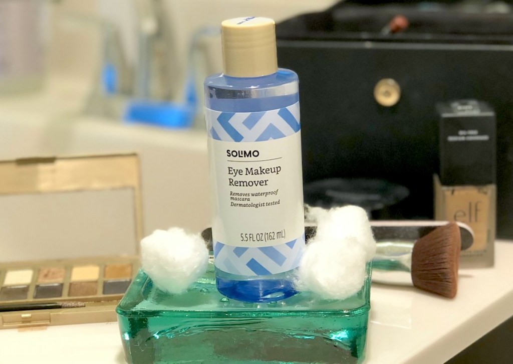 blue bottle of Solimo Amazon makeup remover sitting on bathroom counter with various types of cosmetics