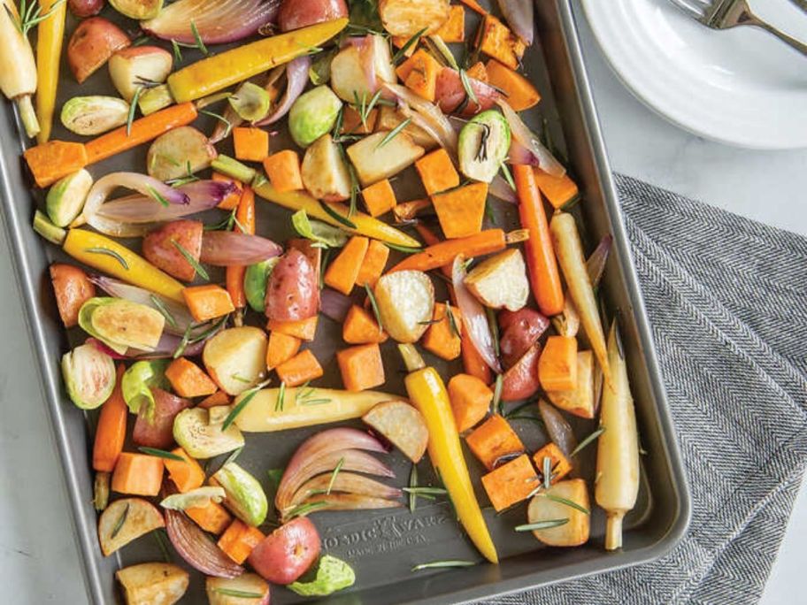 roasted vegetables on a baking sheet resting on a towel next to a plate with a fork