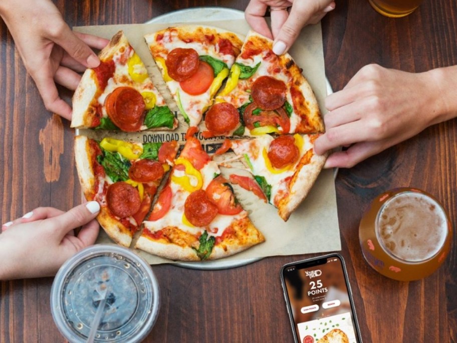 four hands pulling apart a pizza