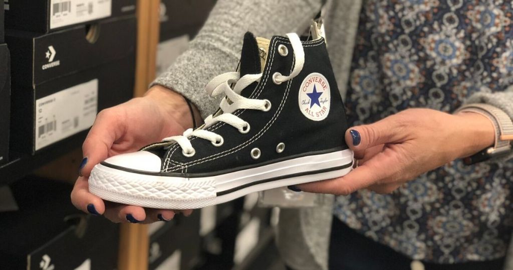 woman's hands holding one left foot adult converse high top sneaker