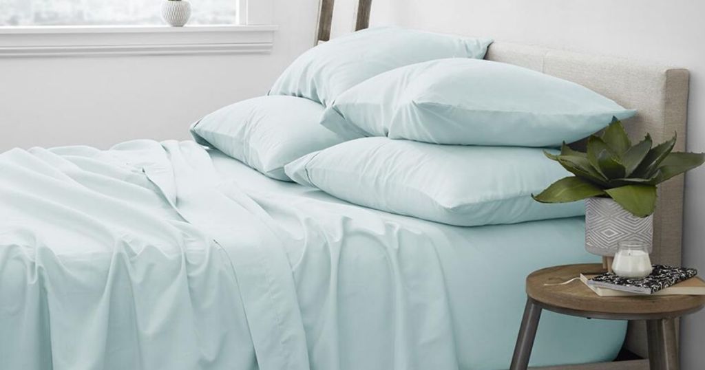 bed made with just sheets and four pillows, end table next to bed with small potted plant on it