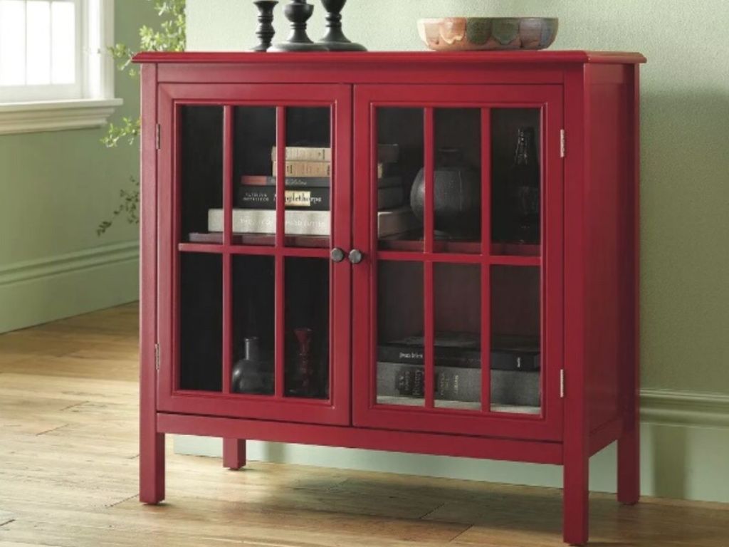 two door wooden cabinet with glass windows on each door topped with candlesticks and decorative bowl