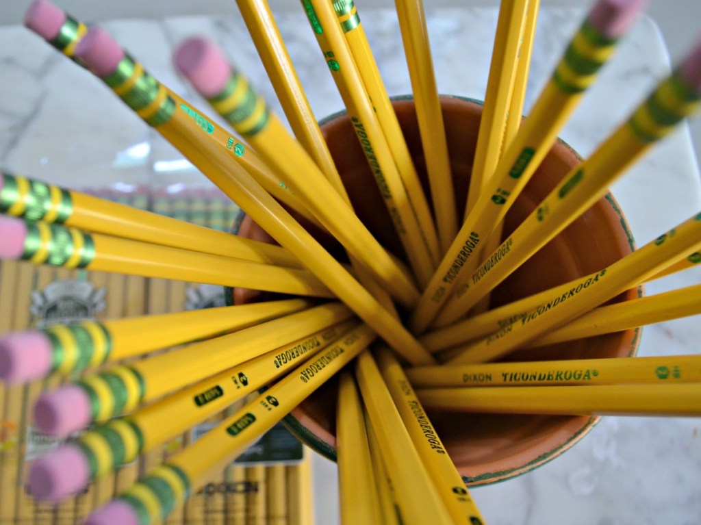 many pencils in cup and package of pencils on table