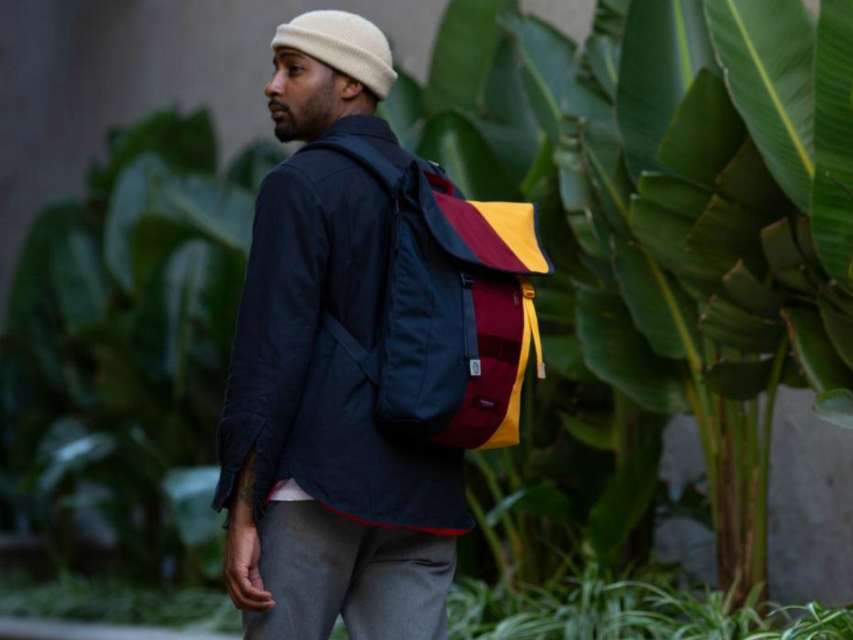 man walking by foilage wearing colorful backpack
