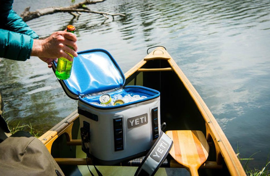 man grabbing water bottle from a YETI cooler on a canoe