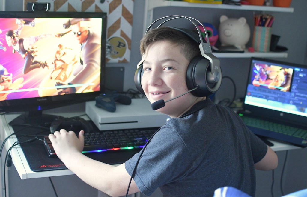 boy smiling wearing headphones sitting at desk with computer gaming setup