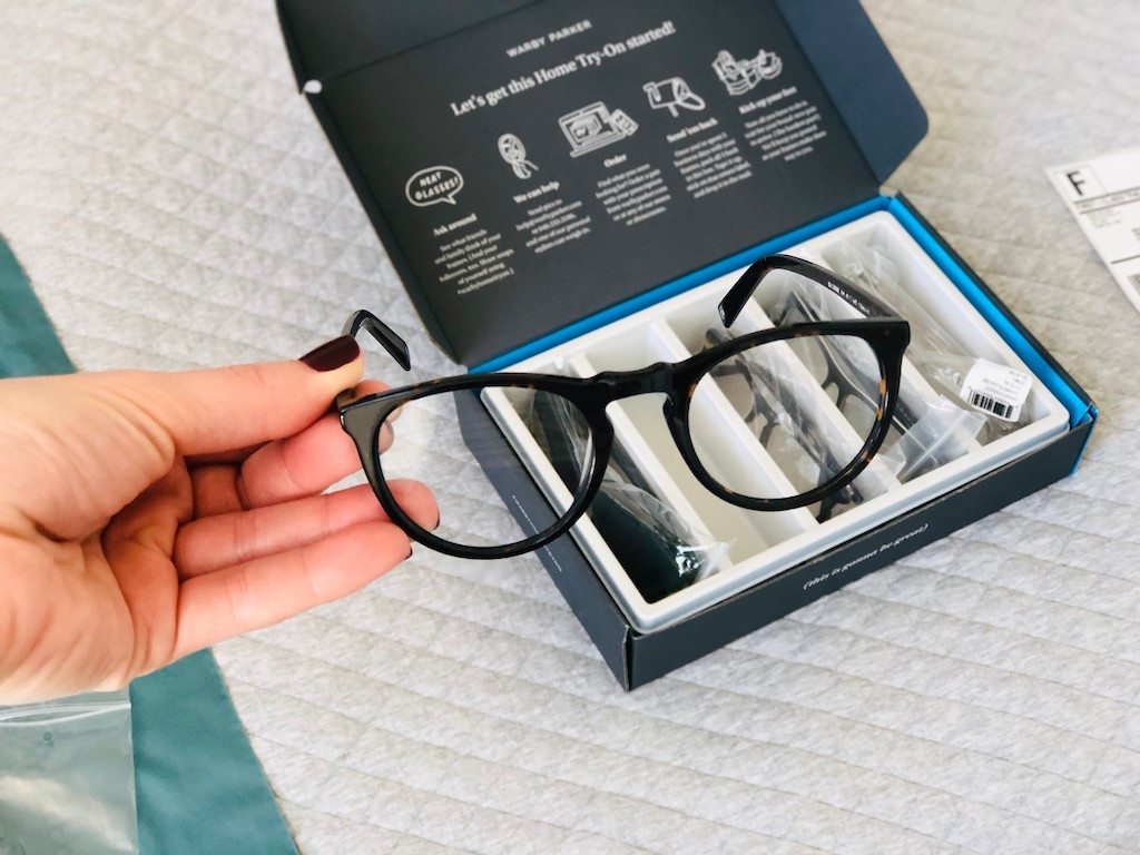 holding eyeglasses in front of a Warby Parker box 