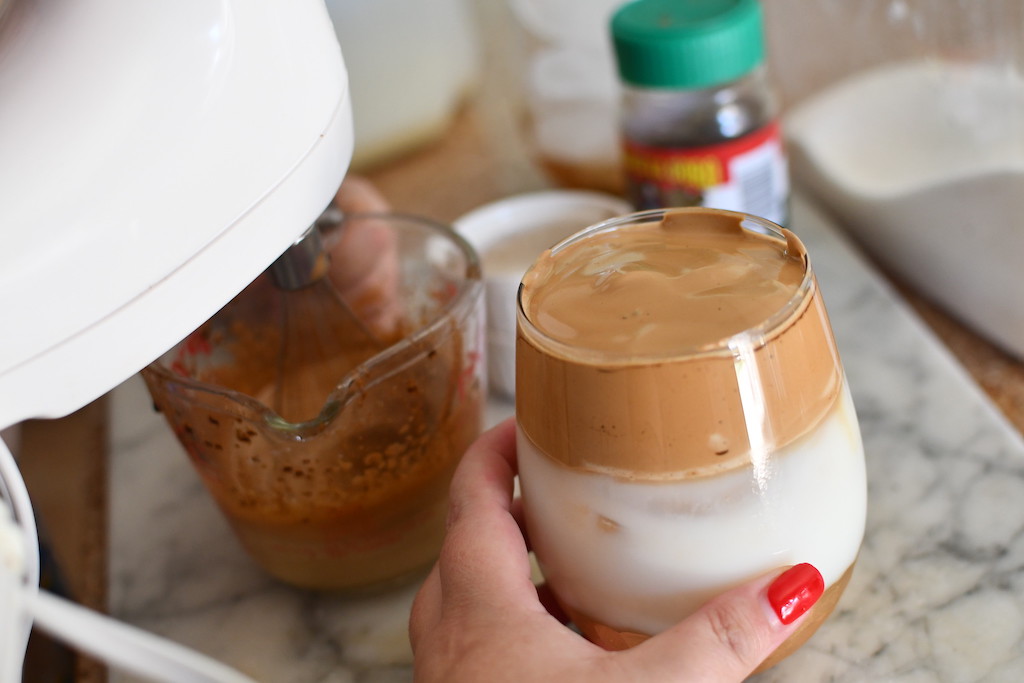 holding whipped iced coffee in cup with mixer in the background